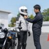 教習所でフルフェイスヘルメットを確認する日本人初心者と指導員